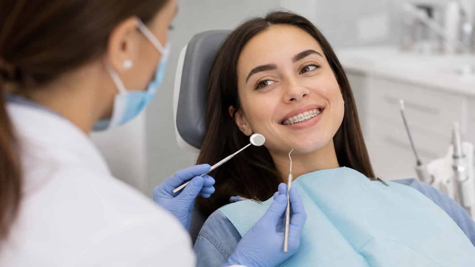 Smiling woman with clear aesthetic ceramic brackets on her teeth during a dental checkup with a dentist in a bright clinic.