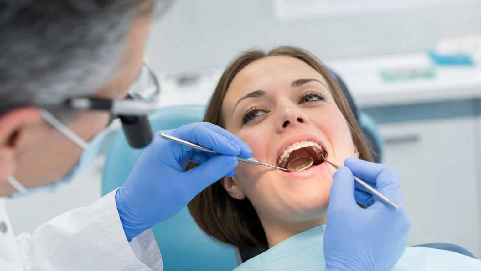 Dentist using a mirror and probe to examine lingual brackets attached to the inner surface of a patient's teeth.